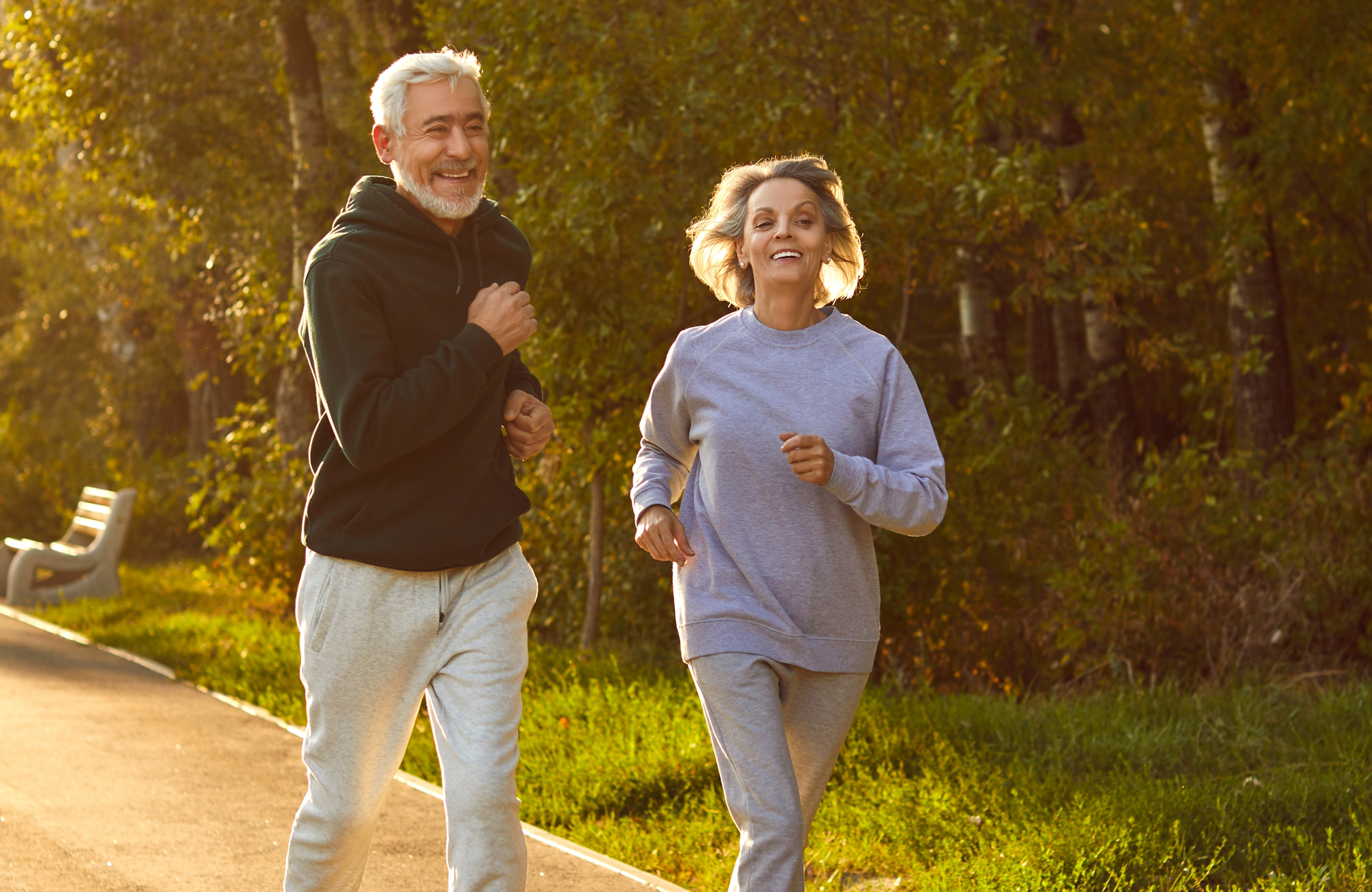 Older couple jogging together along a sunlit park path