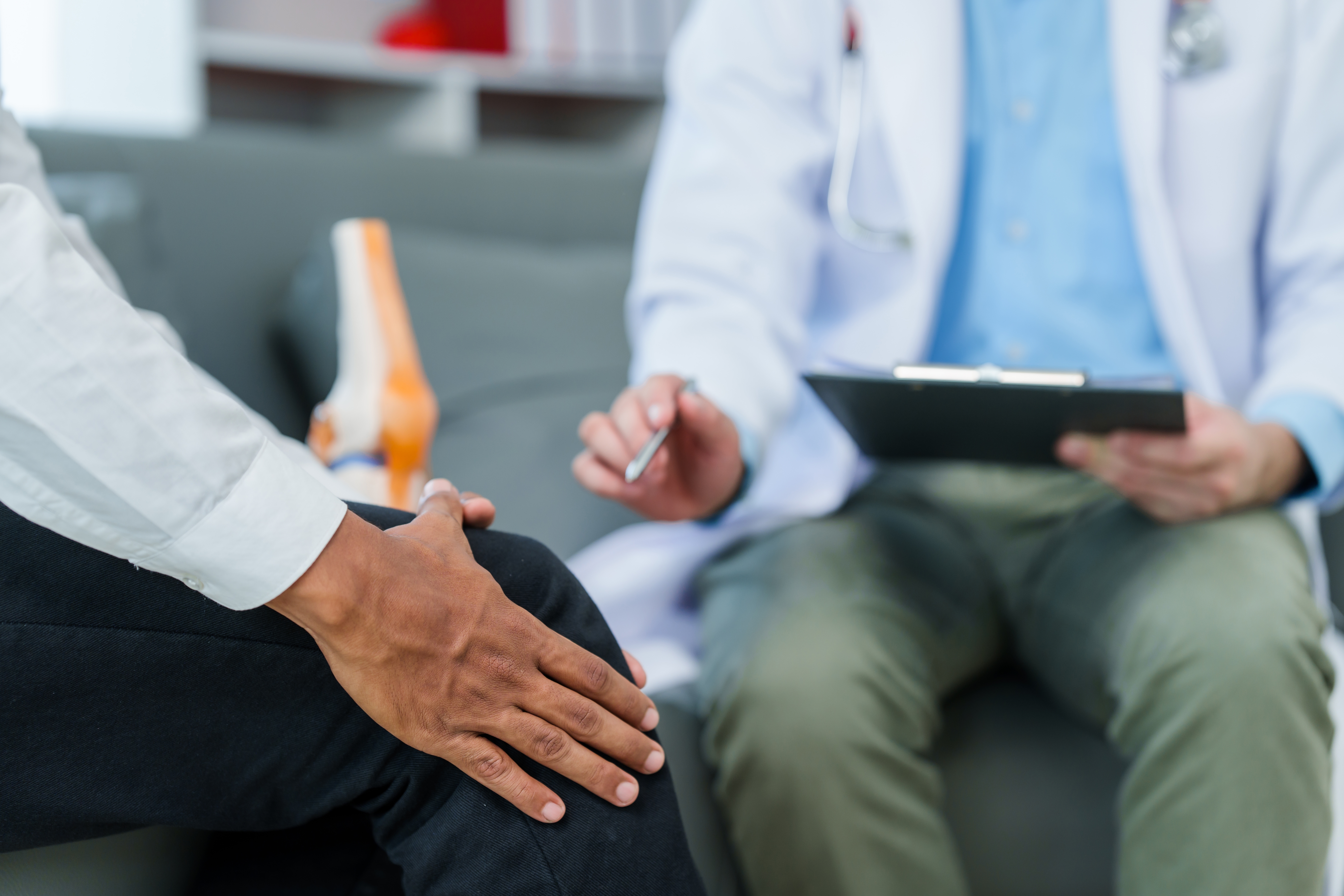 Physician taking notes during a consultation with a patient about joint pain