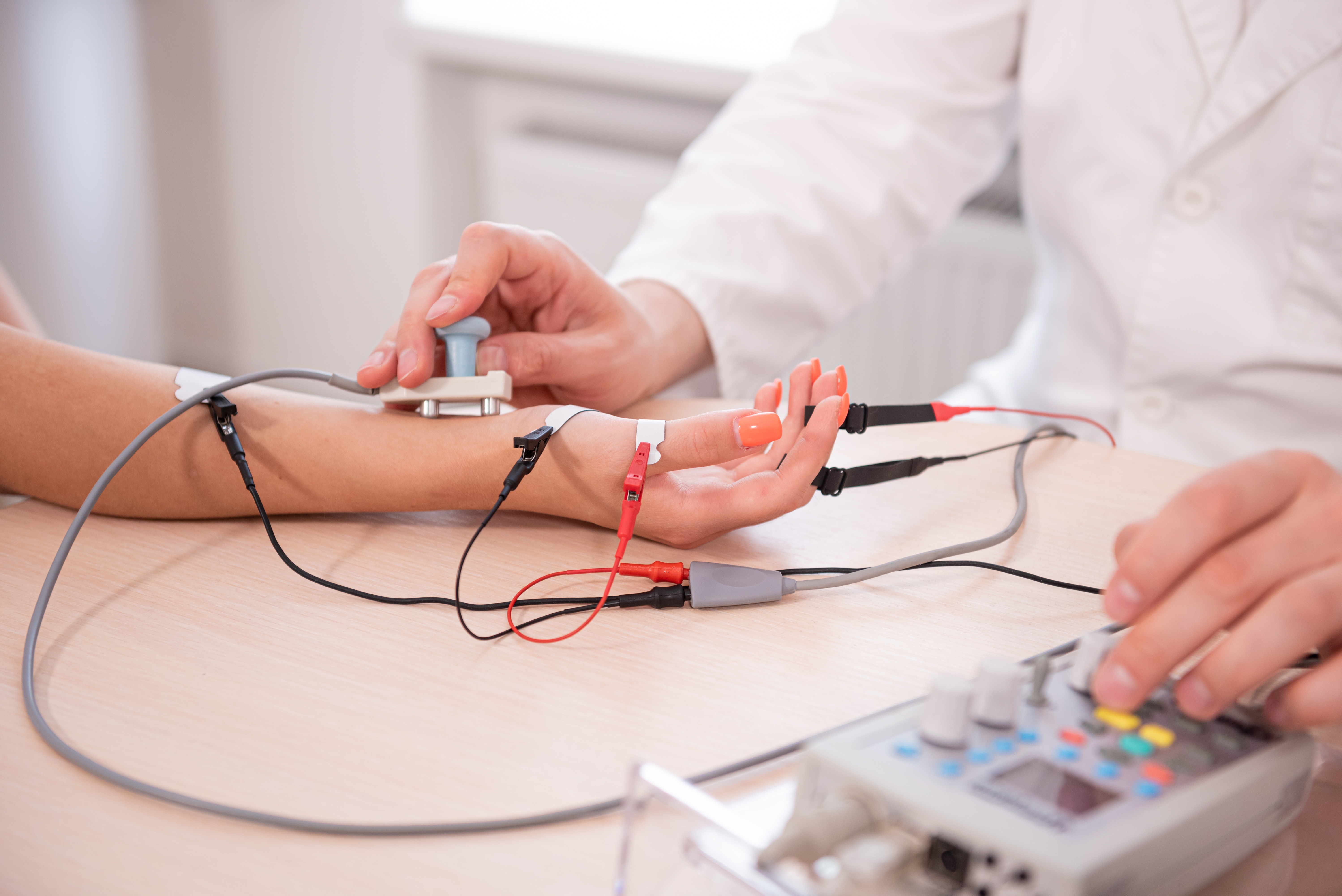 Clinician performing a nerve conduction study, with electrodes placed along a patient's forearm and hand